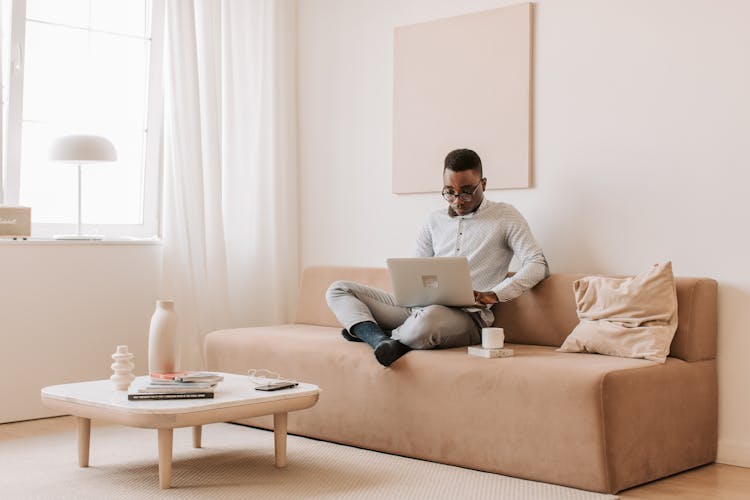 A Man Sitting On A Sofa Working With A Laptop