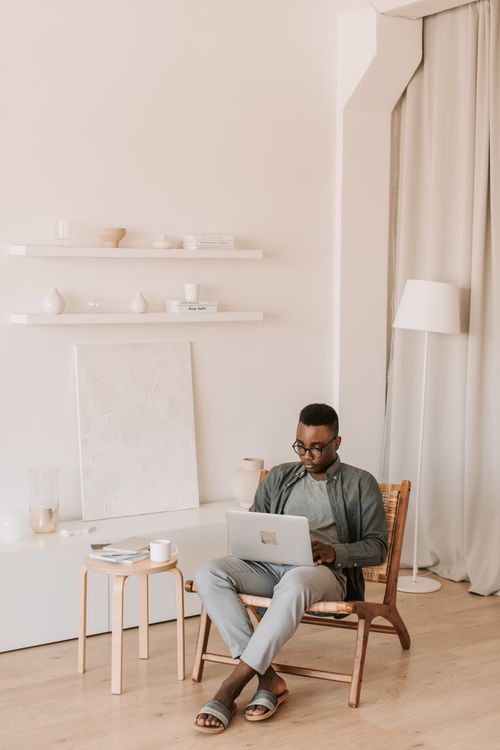 Free A man in a minimalist living room works on a laptop, embodying the modern work-from-home lifestyle. Stock Photo