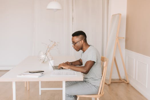 Young man in gray shirt working on a laptop indoors, embodying modern remote work lifestyle.