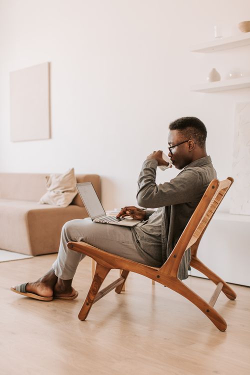 Free A man enjoys a cup of coffee while working remotely on a laptop indoors in a cozy setting. Stock Photo