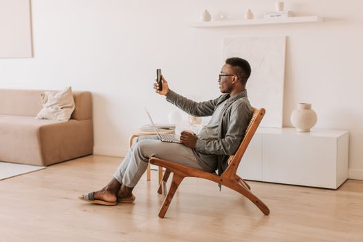 A man enjoys a comfortable video call at home using a smartphone and laptop. Modern and serene indoor setting.