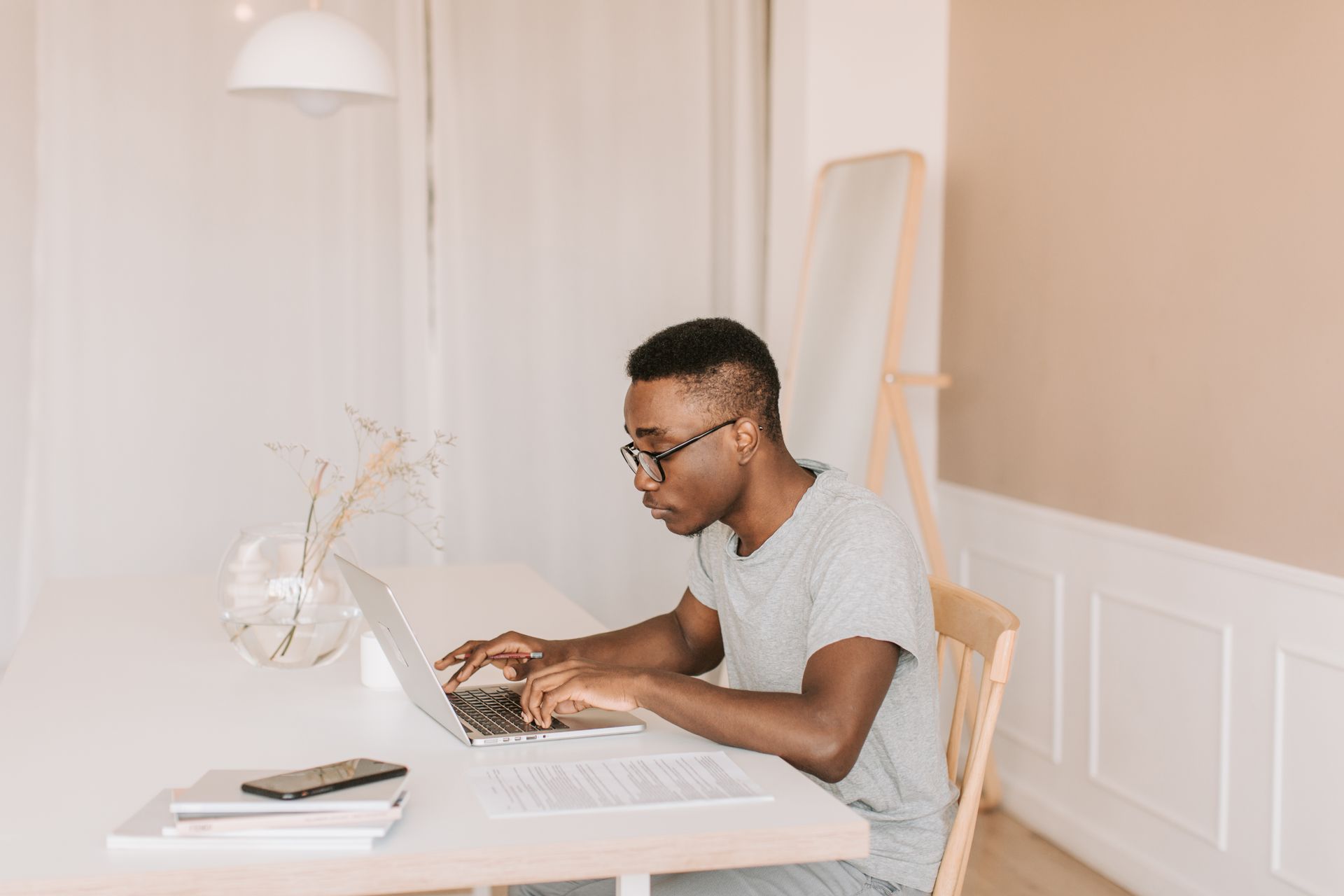 Adult man working from home, typing on laptop in a bright, modern home office setting.