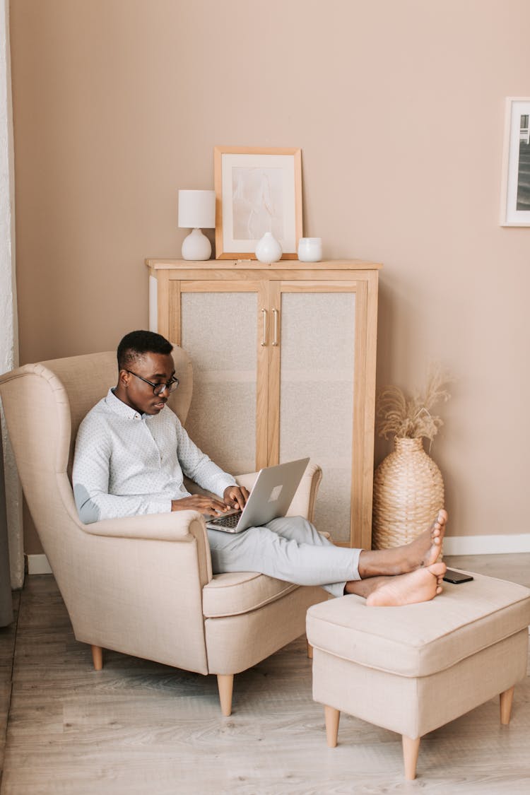 A Man In Gray Shirt Using A Laptop While Sitting On The Sofa