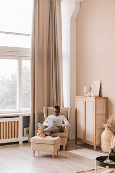African American man working on laptop in a stylish living room, embracing remote lifestyle.