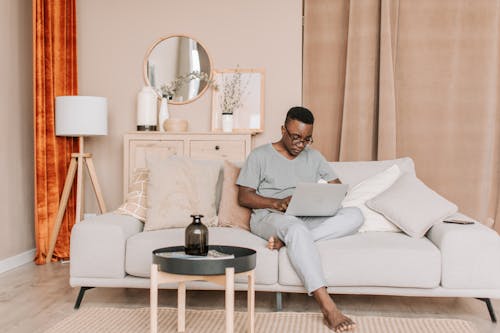 A Man in Gray Shirt Using a Laptop while Sitting on the Sofa