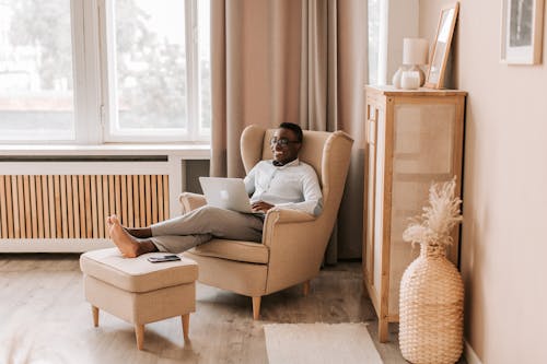 A Man in Gray Shirt Using a Laptop while Sitting on the Sofa