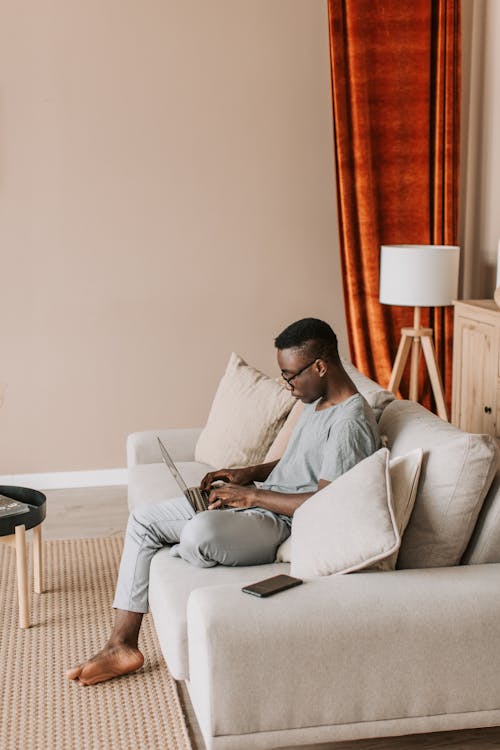 A Man in Gray Shirt Using a Laptop while Sitting on the Sofa