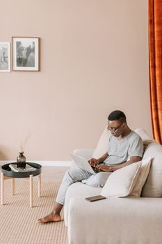 African American man working on a laptop in a modern living room setting.