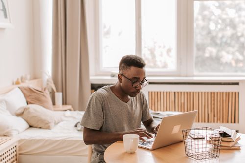 Free A man working on a laptop in a cozy bedroom setting, epitomizing remote work lifestyle. Stock Photo