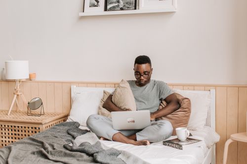Free Adult man working from bed with laptop, relaxing in comfortable home setting. Stock Photo