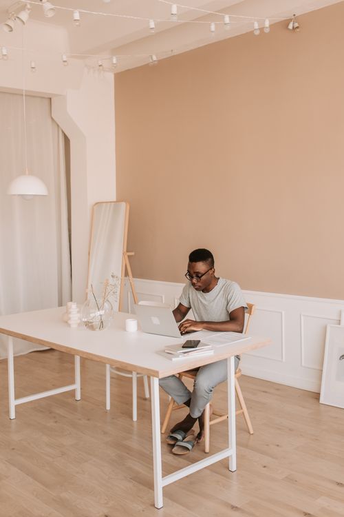 Free Man working on a laptop in a minimalist home office with natural lighting. Stock Photo