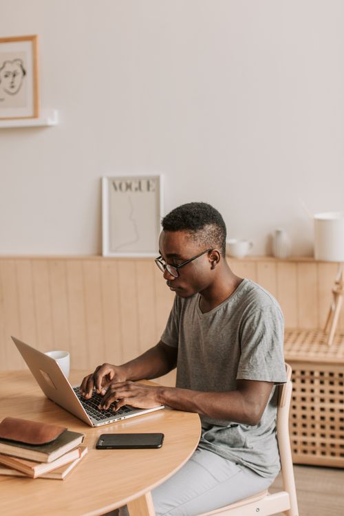 Free Man typing on a laptop indoors, symbolizing modern remote work and online learning. Stock Photo