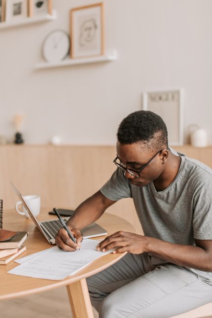 Adult man concentrating on studies at home, using laptop and writing notes at a desk. Adult man concentrating on studies at home, using laptop and writing notes at a desk.