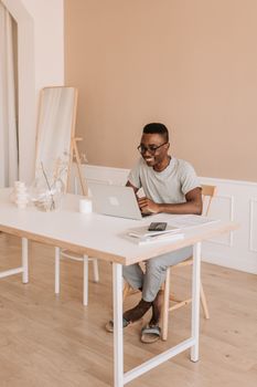 Man smiling while working on a laptop in a cozy home office with contemporary decor.