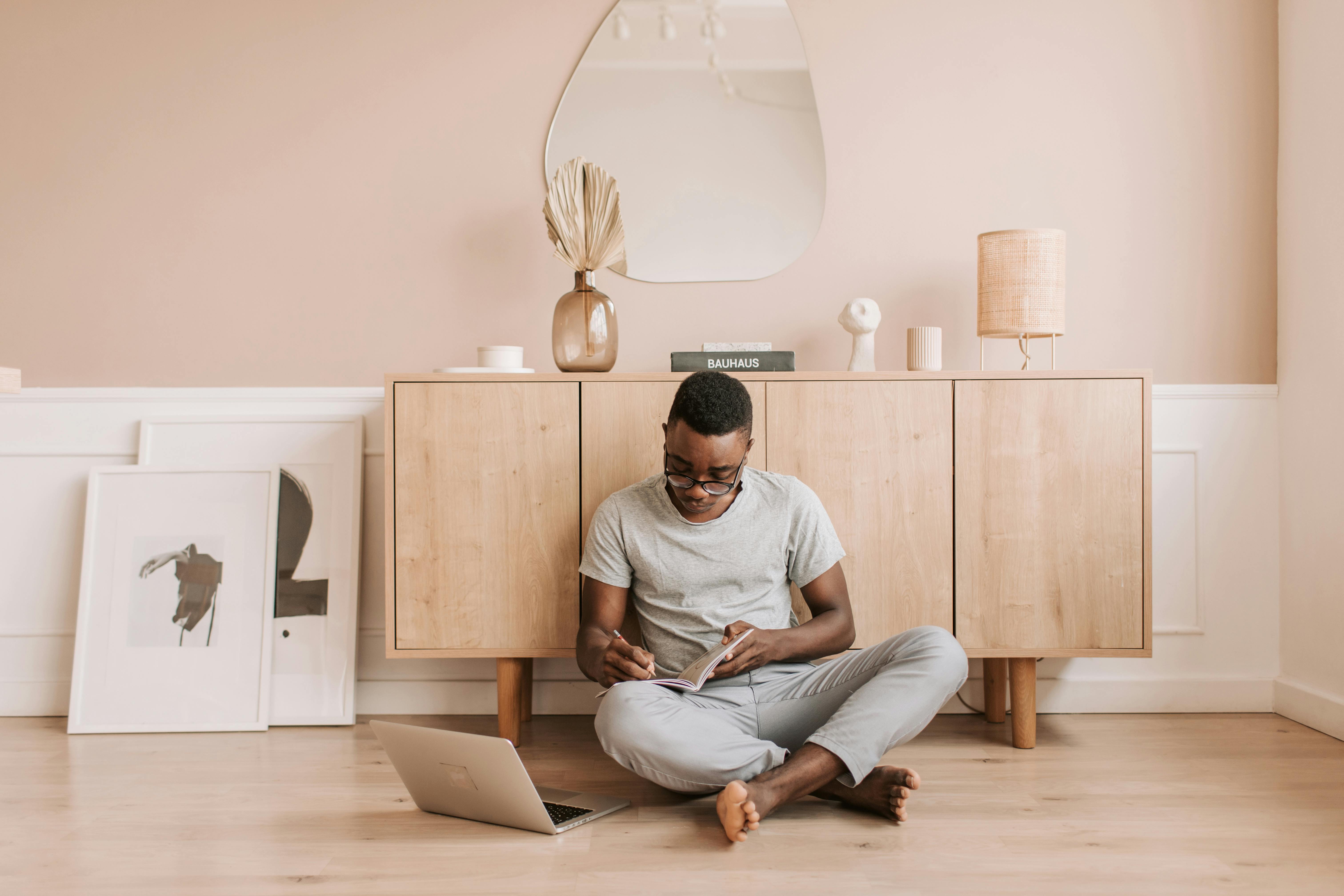 Free Young man sitting on floor taking notes with a laptop in his stylish, modern home office. Stock Photo