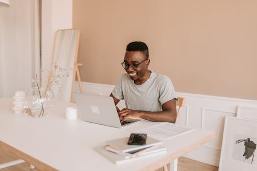 Happy young man typing on laptop in bright modern home office, enjoying his work.