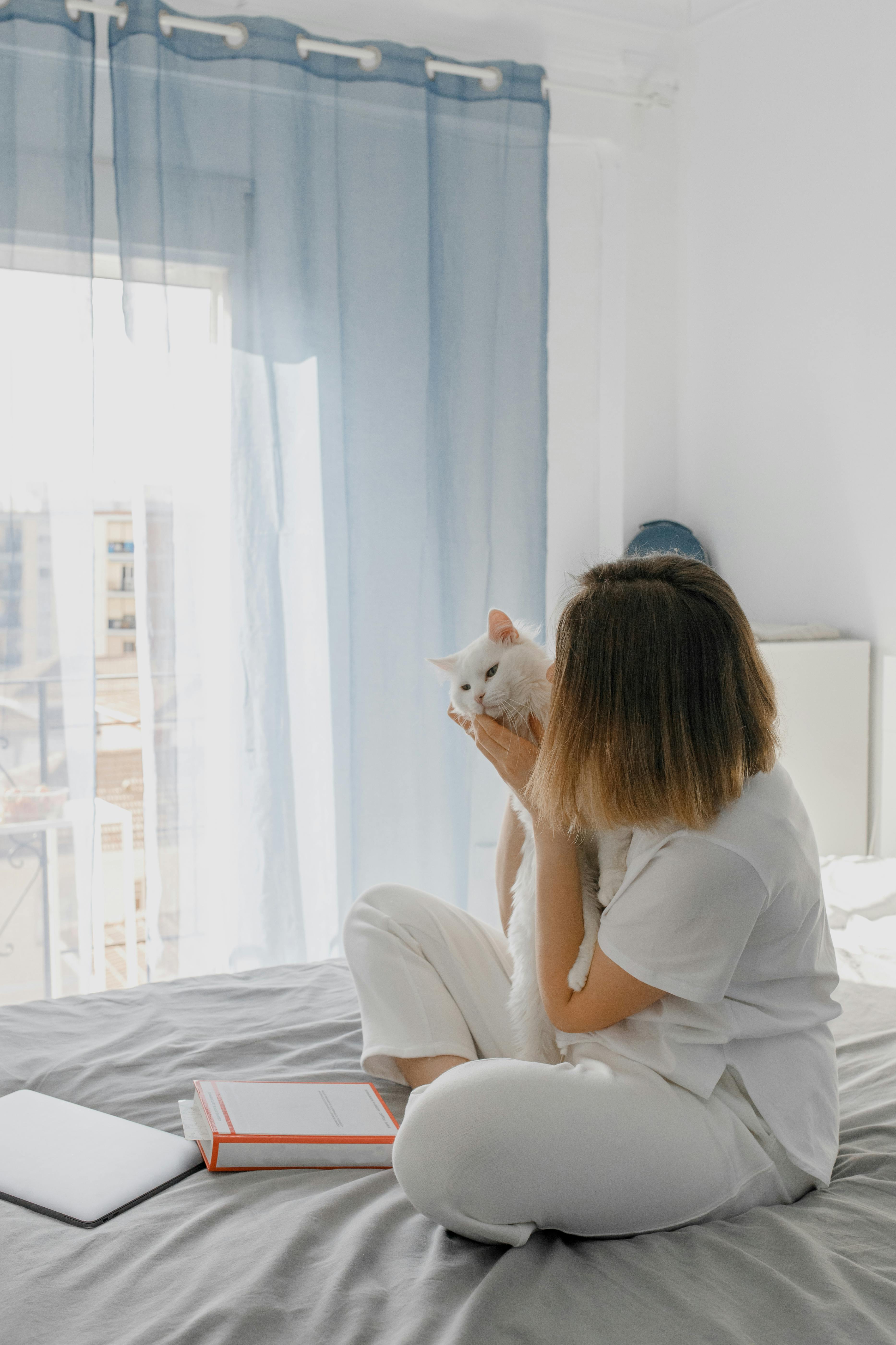 Person in white shirt sitting on bed while hugging a cute cat