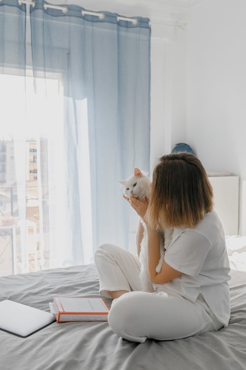 Person in White Shirt Sitting on Bed while Hugging a Cute Cat