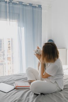 在明亮的室内空间里，一名妇女坐在床上，慈爱地抱着她的猫