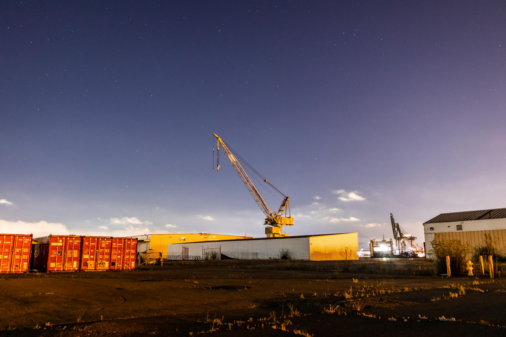 An industrial scene with cranes and cargo containers under a starry night sky, illuminating port operations.