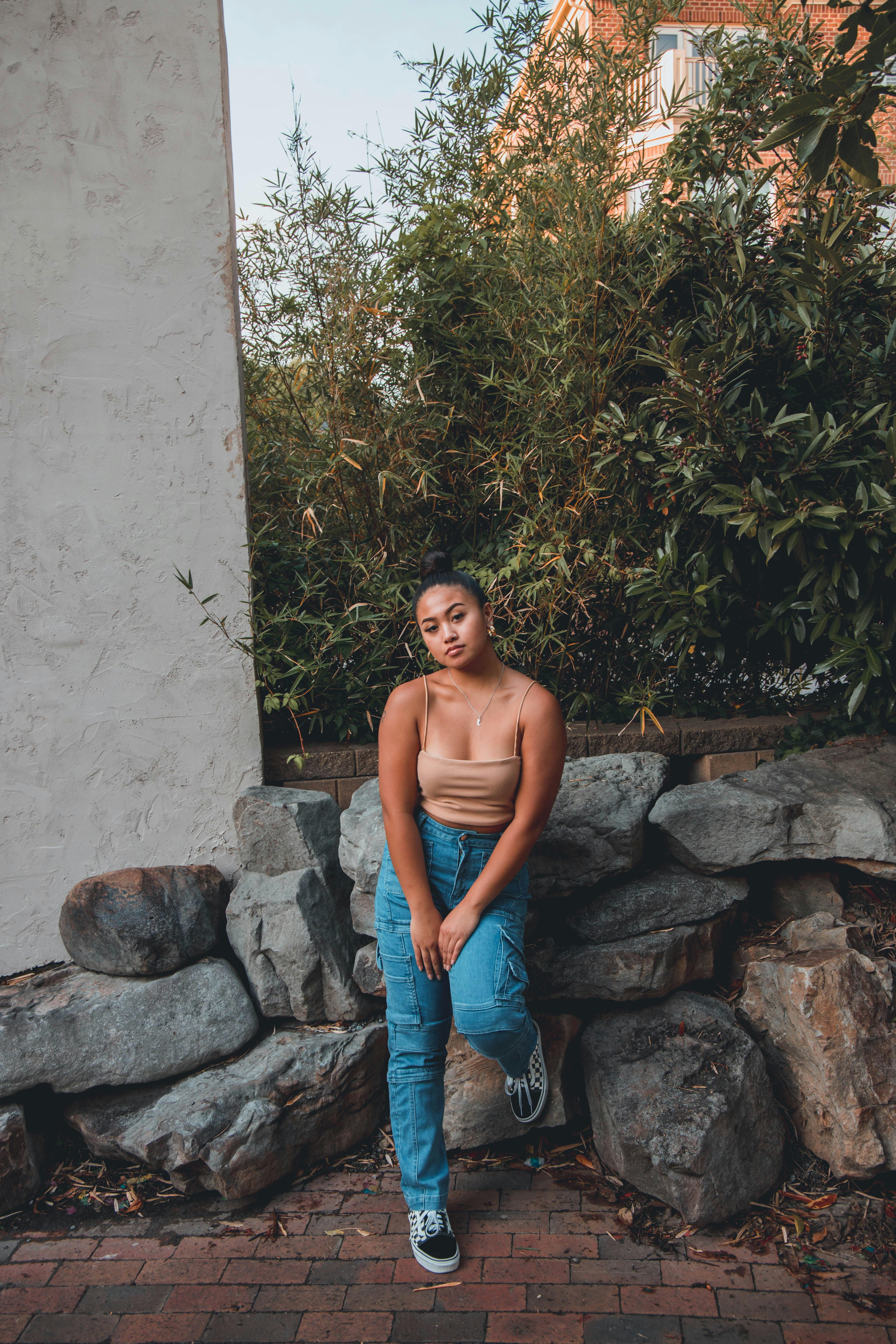 Free Stylish woman in urban setting, posing on rocks in denim jeans and casual top. Stock Photo