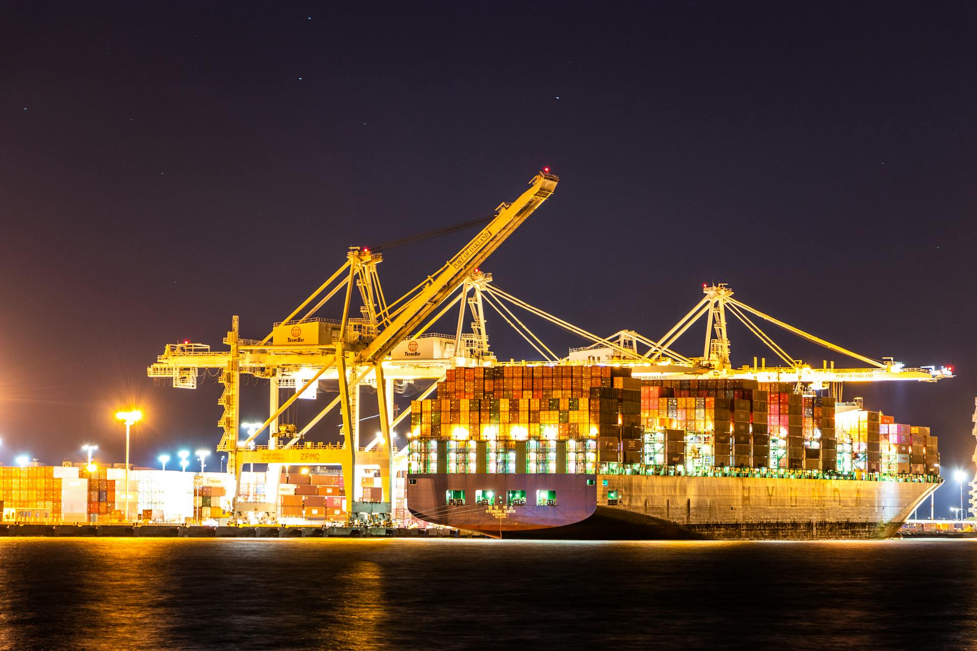 A large container ship illuminated by lights at a busy port with cranes at night.