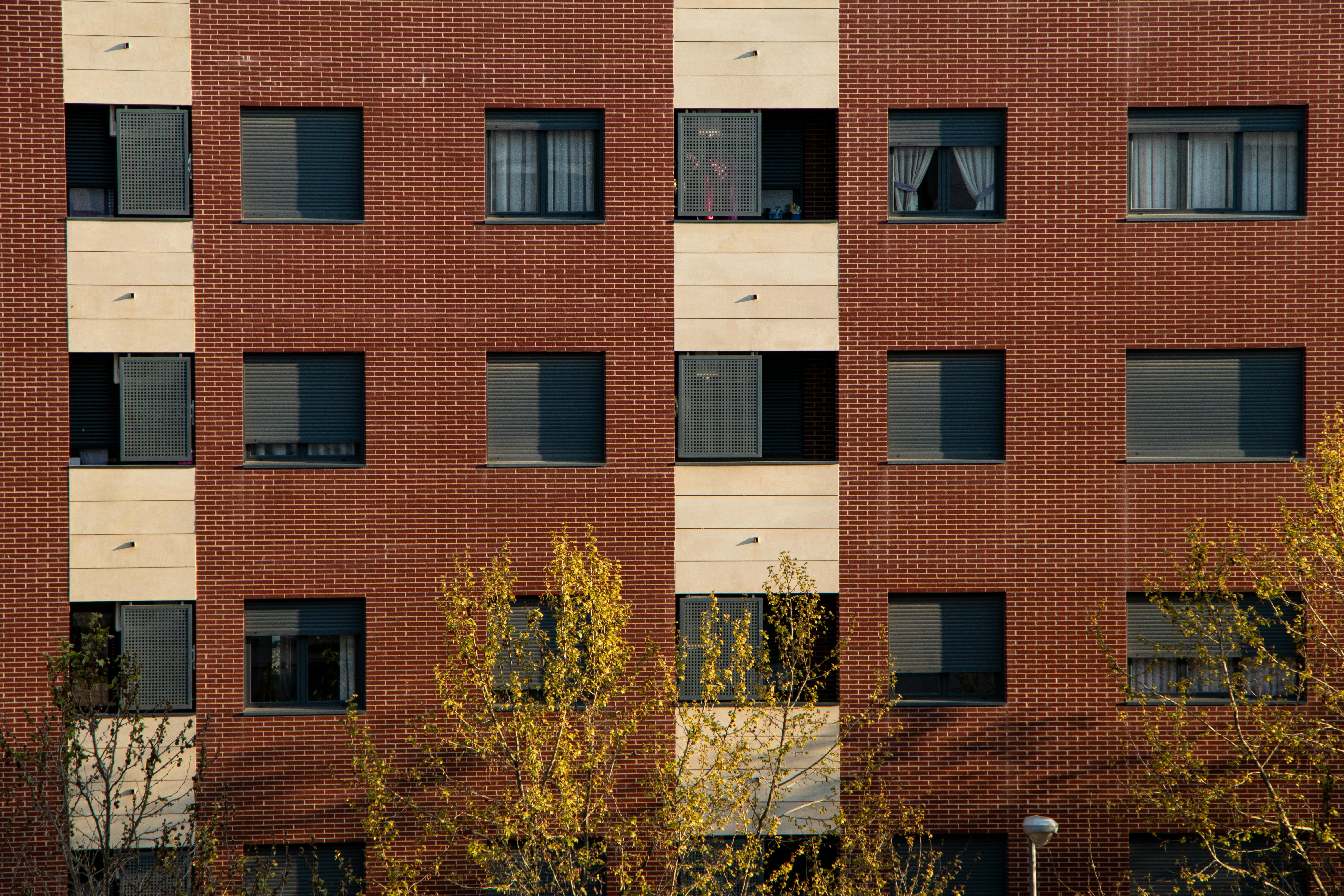 Close-up of a brick and concrete residential building facade in Logroño with symmetrical windows and trees below.