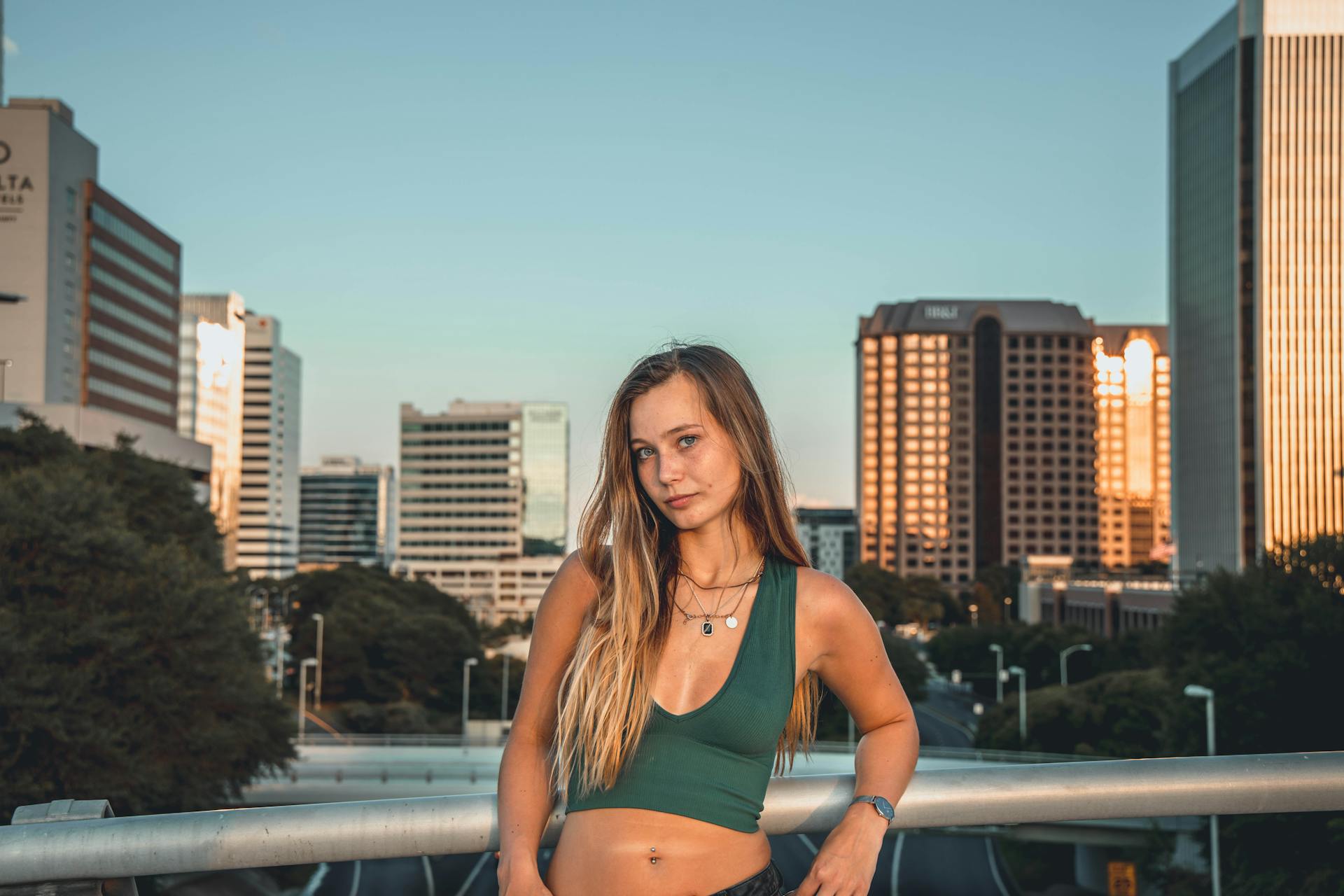 A woman in a crop top poses against an urban skyline during sunset, capturing city vibes.