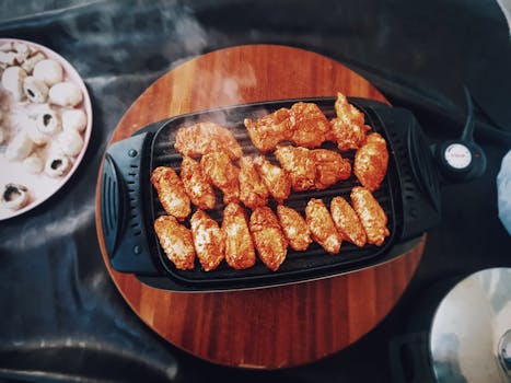 Top view of delicious spicy chicken wings grilling on an electric grill with mushrooms nearby.