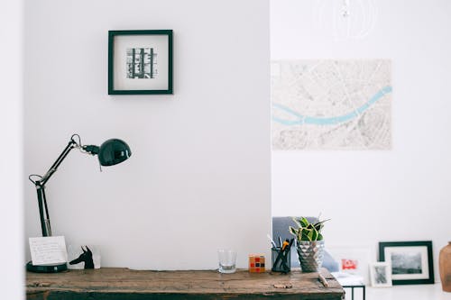 Lamp with cup of stationery placed on wooden desk with potted plant in light cozy apartment