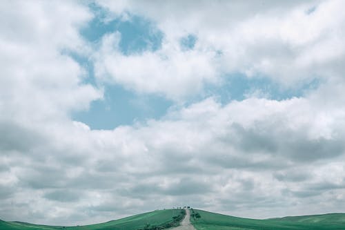 Picturesque scenery of fluffy cumulus clouds floating in blue sky over narrow road going through grassy mountainous terrain
