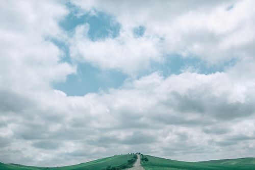 Free Picturesque scenery of fluffy cumulus clouds floating in blue sky over narrow road going through grassy mountainous terrain Stock Photo