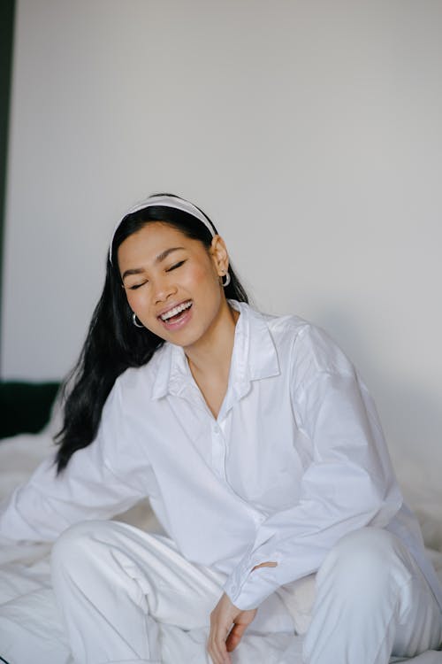 Позитивная молодая этническая женщина улыбается с закрытыми глазами на кровати