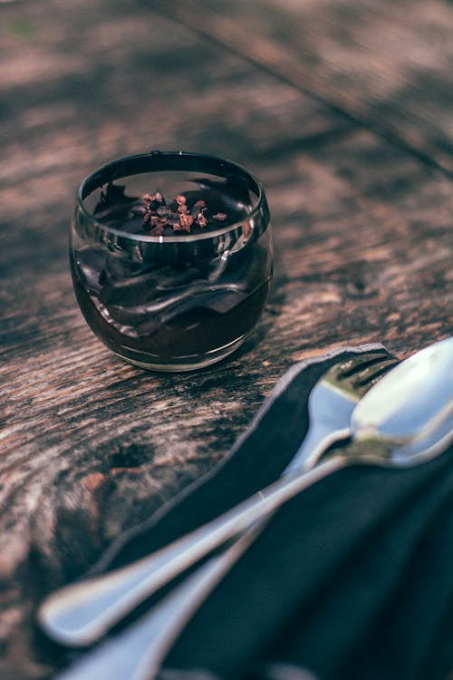 From above of appetizing chocolate mousse in glass cup served on wooden table with silver cutlery in cafe