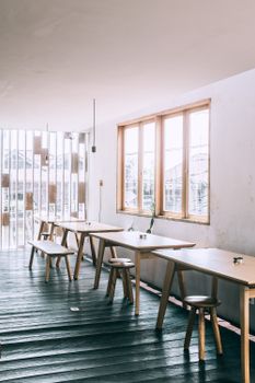 Interior of cozy spacious cafe with wooden tables and stools placed near window in daylight