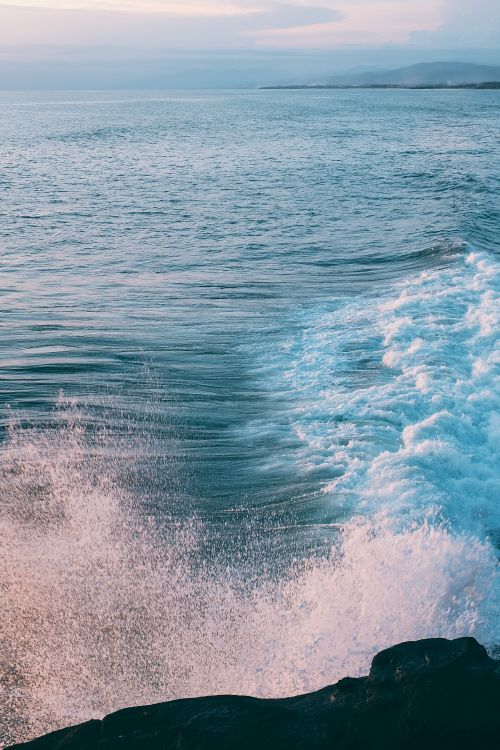 Free Picturesque scenery of powerful ocean with foamy waves crashing on rocky cliff against cloudy sunset sky Stock Photo