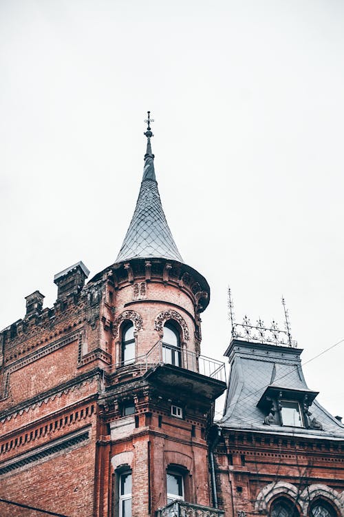 From below exterior of aged Castle of Baron Steingel with brick walls and spire roof against cloudy sky in Kyiv