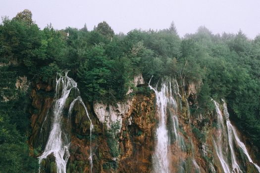 在多云的天空下，风景如画的快速瀑布从覆盖着郁郁葱葱绿树的粗糙岩石悬崖之间流过