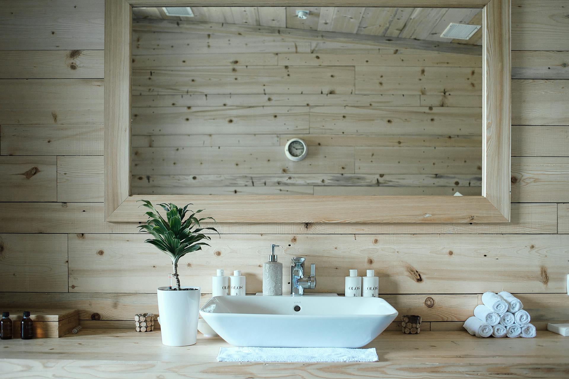 Stylish interior design of contemporary bathroom with wooden walls and big mirror above sink and table with toiletries