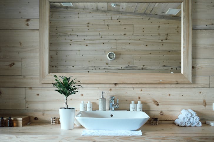 Stylish interior design of contemporary bathroom with wooden walls and big mirror above sink and table with toiletries