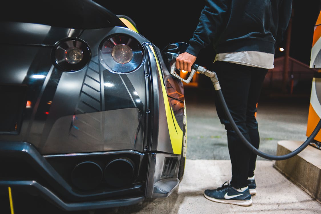 Side view of crop unrecognizable male refueling modern racing automobile in petrol station in evening