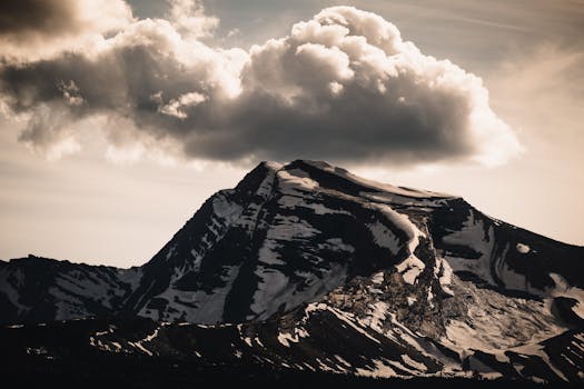 A stunning snow-capped mountain peak under a dramatic cloud formation, perfect for nature photography enthusiasts.
