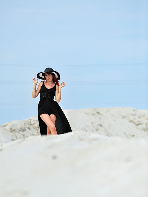 Free Stylish woman posing in a black dress and sun hat on sandy landscape. Stock Photo