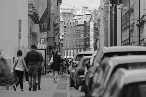 Black and white unrecognizable passers by strolling on paved sidewalk along narrow road in old city district