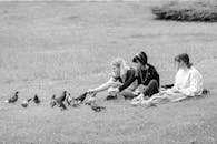 Content girlfriends resting on grassy lawn and feeding pigeons