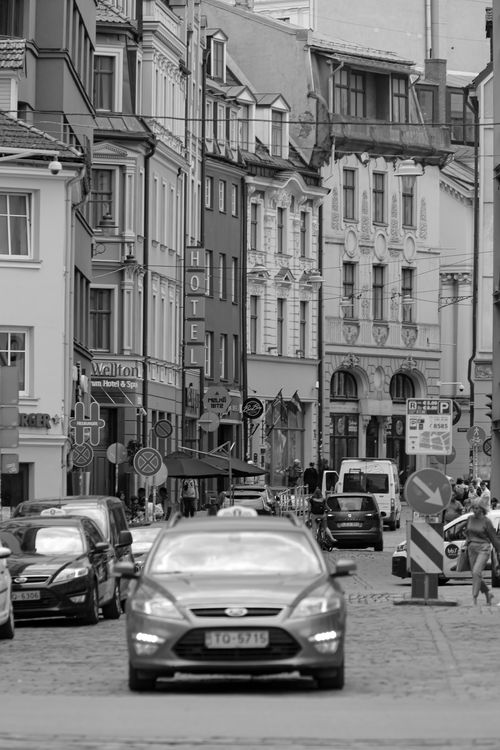 Free Black and white narrow street in downtown with cars driving down road surrounded by old buildings Stock Photo