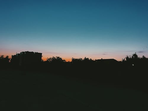 Light blue morning sky illuminated by rising sun above silhouettes of small town buildings and trees