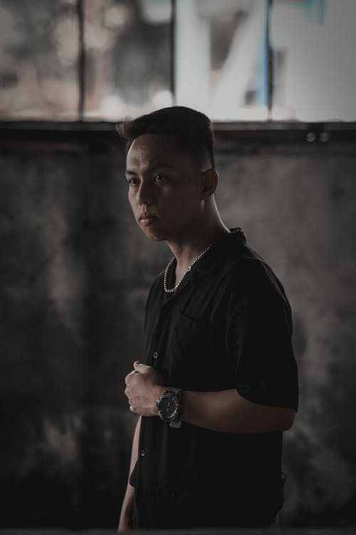 Focused young ethnic man standing in dark abandoned building and looking away