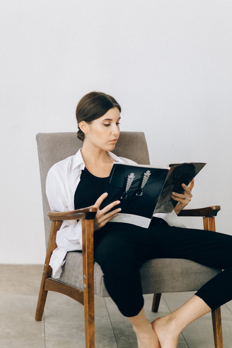 Woman Sitting On A Chair Reading A Magazine