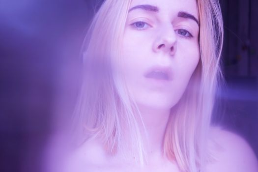Romantic young female model with long blond hair and dark eyebrows enticing while looking at camera with smoke effect